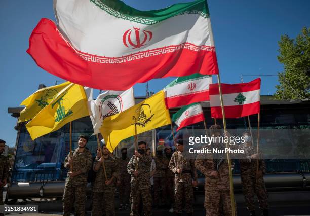 Members of the Basij paramilitary force hold Iranian flag, Lebanese flag, flag of Hashd Shabi, flag of Quds force's Fatemiyoun Brigade, and a flag of...