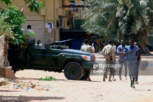 People run past a military vehicle in Khartoum on April 15 amid reported clashes in the city. Sudan's paramilitaries said they were in control of...