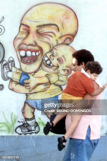 Woman holding her son walks in front of a mural of Brazilian soccer starn Ronaldo, and his son Ronald, 07 June 2002, on a street in Rio de Janeiro,...