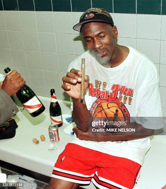 Michael Jordan of the Chicago Bulls enjoys a cigar in the locker room 14 June after winning game six of the NBA Finals against the Utah Jazz at the...
