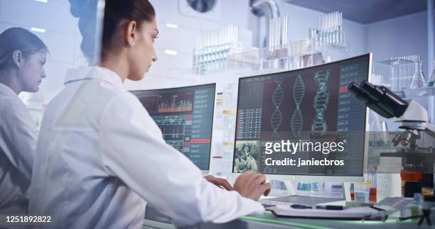 vrouwelijk onderzoeksteam dat dna-mutaties bestudeert. computerschermen met de helix van dna in voorgrond - medical test stockfoto's en -beelden