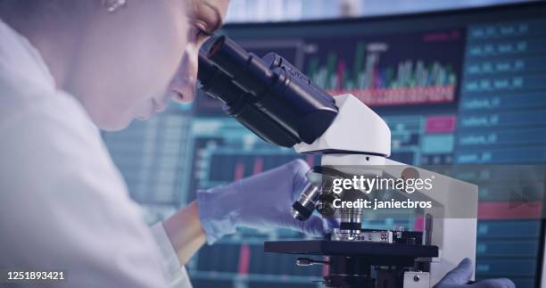 atractiva científica femenina durante la investigación. uso del microscopio en laboratorio futurista - microbiologist fotografías e imágenes de stock