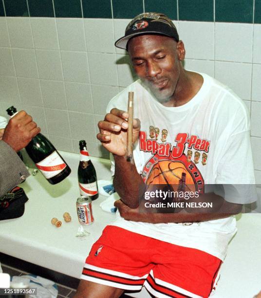 Michael Jordan of the Chicago Bulls enjoys a cigar in the locker room 14 June 1998 after winning game six of the NBA Finals against the Utah Jazz at...