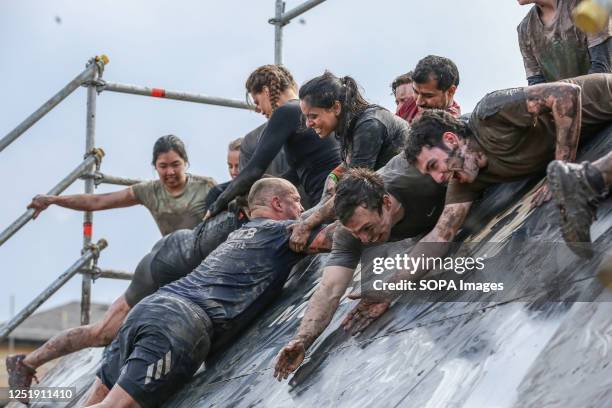 Participants try to climb up on a slippery surface during Tough Mudder race in Finsbury Park, London. Tough Mudder was co-founded by Will Dean and...