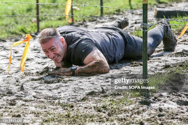 Participant crawls underneath wires during Tough Mudder race in Finsbury Park, London. Tough Mudder was co-founded by Will Dean and Guy Livingstone...