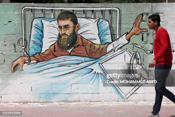 Palestinian man walks past a graffiti of Khader Adnan, a hunger-striking Palestinian imprisoned in an Israeli jail, in Gaza City on April 17, 2023.