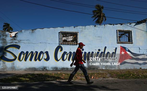Man walks past a graffiti reading "We are Continuity" next to an image of a Cuban flag in a street of Havana on April 17, 2023.