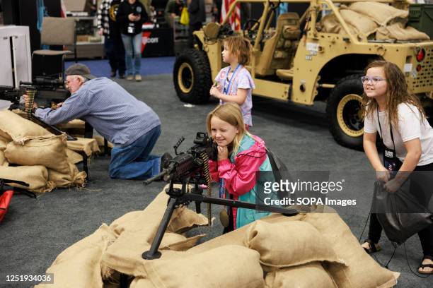 Girl looks through the sights of a machine gun during the National Rifle Association's Annual Meetings & Exhibits at the Indiana Convention Center in...
