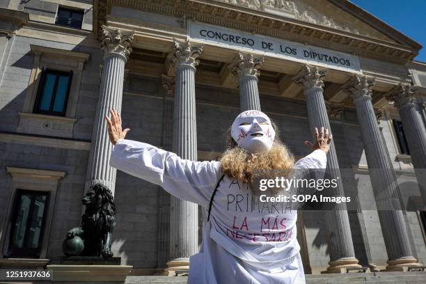 Doctor wearing a mask and gown stands in front of the Congress of Deputies with her arms raised in anger and confrontation during the demonstration....