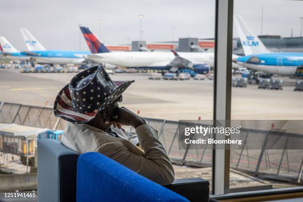 Passenger wearing a hat featuring the design of the US national flag watches aircraft from a window at Schiphol Airport in Amsterdam, Netherlands, on...