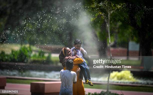Family enjoys water jet from water sprinklers on a hot day at ndia Gate lawn as the temperature rises in the Delhi-NCR on April 18, 2023 in New...