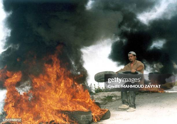 Palestinian man adds car tires to an already burning pile during a protest 18 April 2004 by Palestinian refugees at the Ain el-Helweh refugee camp,...