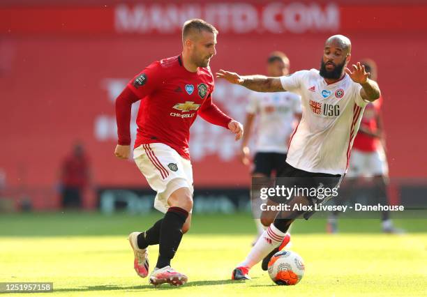 Luke Shaw of Manchester United passes the ball under pressure from David McGoldrick of Sheffield United during the Premier League match between...