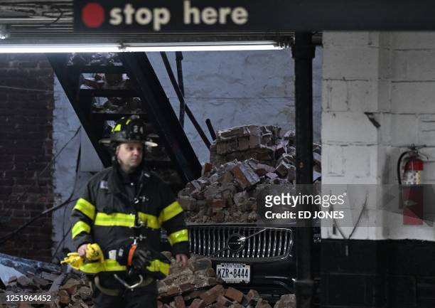 Member of the New York Fire Department walks past a car covered in rubble at the scene of a parking lot collapse in lower Manhattan, New York, April...