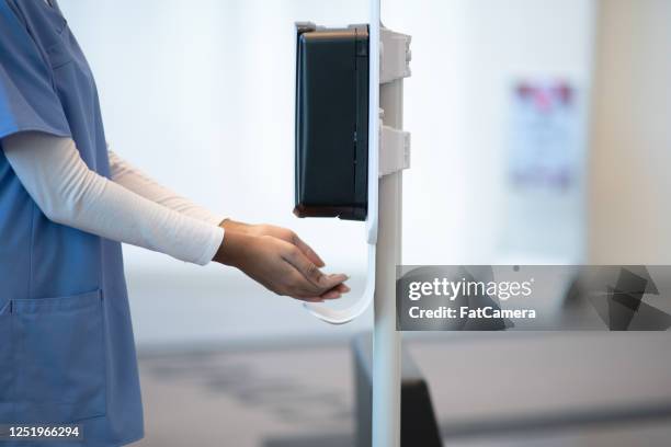 enfermeira usando dispensador de desinfetante para as mãos em clínica - hand sanitiser - fotografias e filmes do acervo