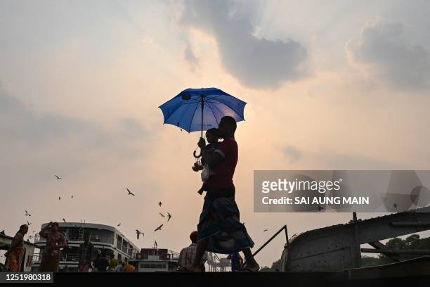 Man carrying his son walks with an umbrella during a heatwave in Yangon on April 19, 2023.