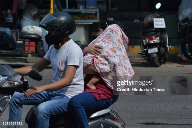 Woman riding pillion covers the head and face of her child in the sweltering afternoon heat as mercury rises higher in the city, in Thane, on April...
