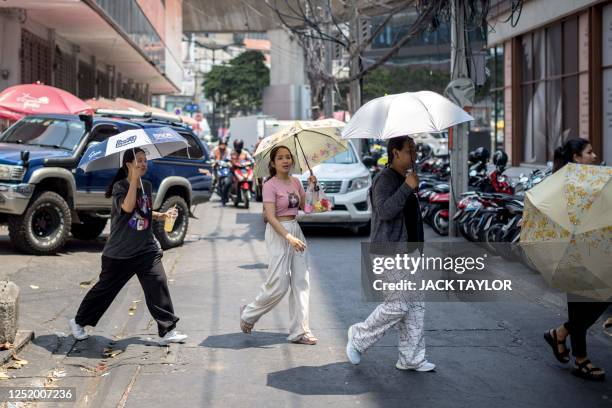 People sheltering from the sun under umbrellas cross a street during heatwave conditions in Bangkok on April 20, 2023. - Sweltering under a...