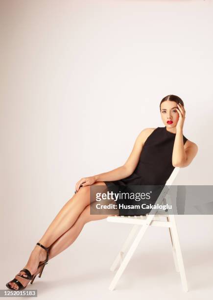 beautiful young woman with mini black dress sitting on white chair front of white background. - mini dress stock pictures, royalty-free photos & images