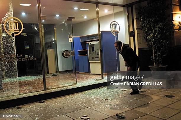 Demonstrator runs by the Galicia Bank Automated Teller Machine, which windows are broken due to stones thrown by workers who protested in Buenos...