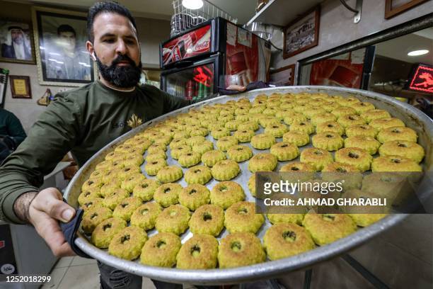 Palestinian baker carries a tray of fresh "maamoul", traditional pastries filled with dates or nuts, on the eve of Eid al-Fitr at the end of Muslim...