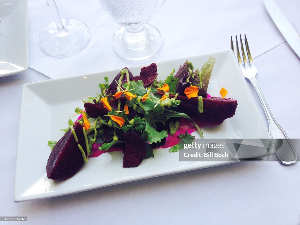Elegant roasted beet salad with arugula, nasturtium flowers and green goddess dressing on a white plate on white butcher paper tablecloth