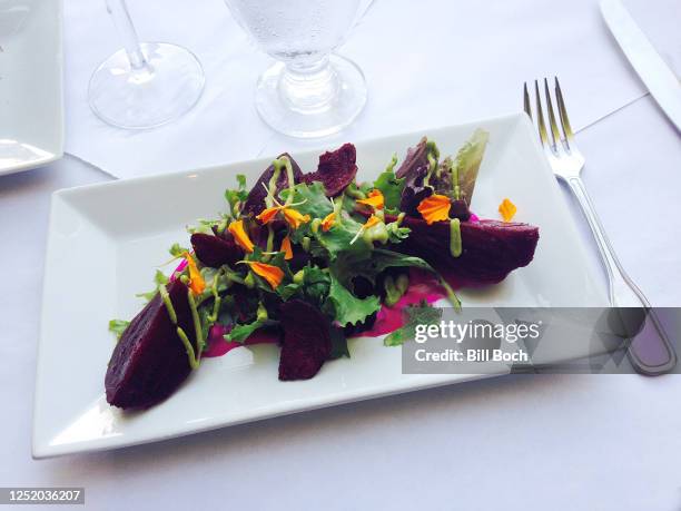 elegant roasted beet salad with arugula, nasturtium flowers and green goddess dressing on a white plate on white butcher paper tablecloth - white butcher paper stock pictures, royalty-free photos & images