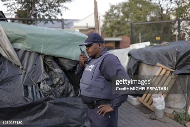 South African Police Service officer talks on the radio at the temporary dwelling built by foreign migrants in front of the United Nations High...