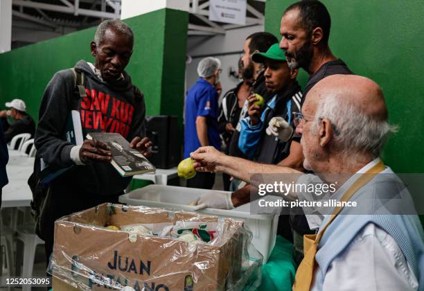 April 2023, Brazil, São Paulo: A man shows a book to priest Julio Lancellotti as he distributes food to people. Lancellotti is known in the South...