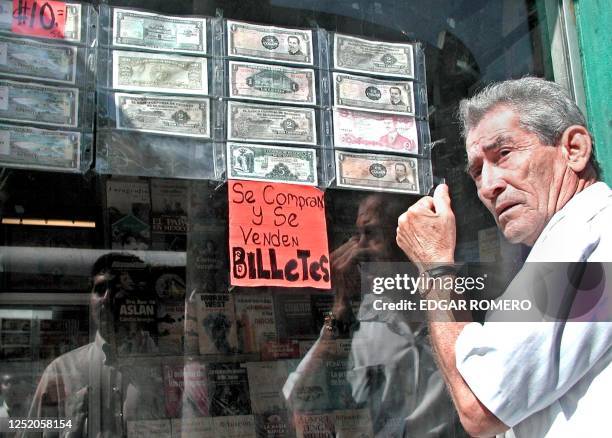 Man looks 18 December 2000 in San Salvador at a window holding various currencies prior to the establishment of a two-currency economy in January...