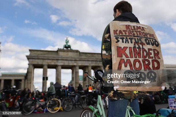 An activist with a banner reading "Climate catastrophe statuesque is child murder" as other activists of the "Last Generation" climate action...