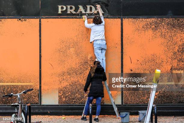 Cleaners scrub off orange paint sprayed by activists from the "Last Generation" climate action movement on a PRADA shop on the famous shopping avenue...