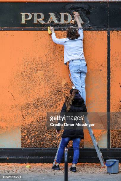 Cleaners scrub off orange paint sprayed by activists from the "Last Generation" climate action movement on a PRADA shop on the famous shopping avenue...