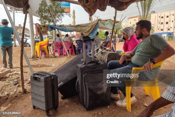 People wait with luggage before boarding a bus departing from Khartoum in the Sudanese capital's south on April 24 as battles rage in the city...