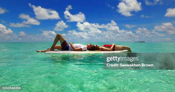 attractive tourist couple sunbathing on the floating paddleboard in the blue ocean water in fiji - fiji relax stock pictures, royalty-free photos & images