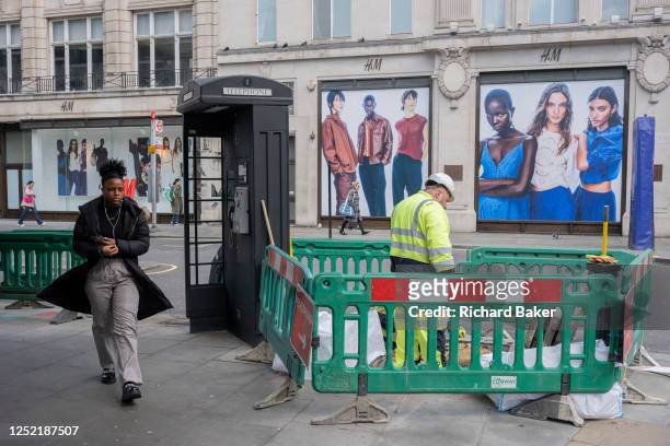 Two contractor workmen attend to their job of street repairs on Oxford Street Street and across the road of a billboard for the high street fashion...