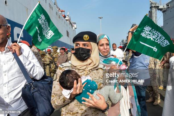 Saudi Navy sailor carries a child as evacuees arrive at King Faisal Navy Base in Jeddah on April 26 following a rescue operation from Sudan. - A ship...