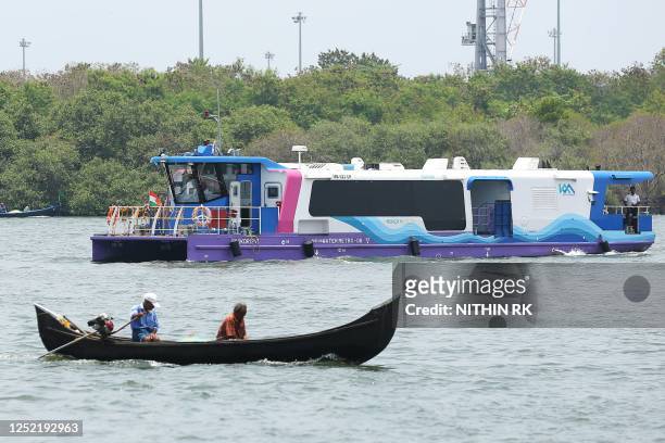 Kochi Water Metro ferry , which are are battery-operated electric hybrid boats, makes its way past fishermen on a boat along the backwaters in Kochi...