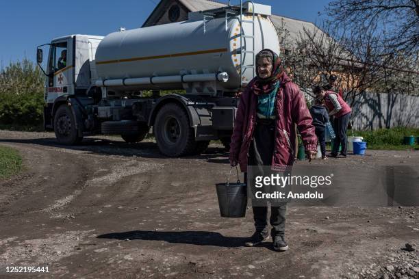 An elderly woman carries a bucket of water that she fills from a Ukrainian Emergency Service water tanker, which travels through the streets of...