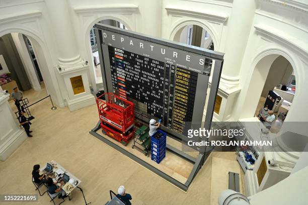 Workers install a Changi Airport flight information analog flipboard at the National Museum in Singapore on April 27, 2023 ahead of an upcoming...