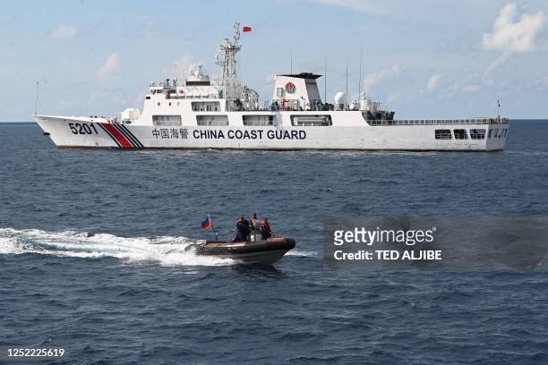 This photo taken on April 23, 2023 shows Philippine coast guard personnel aboard their rigid inflatable boat speeding past a Chinese coast guard ship...