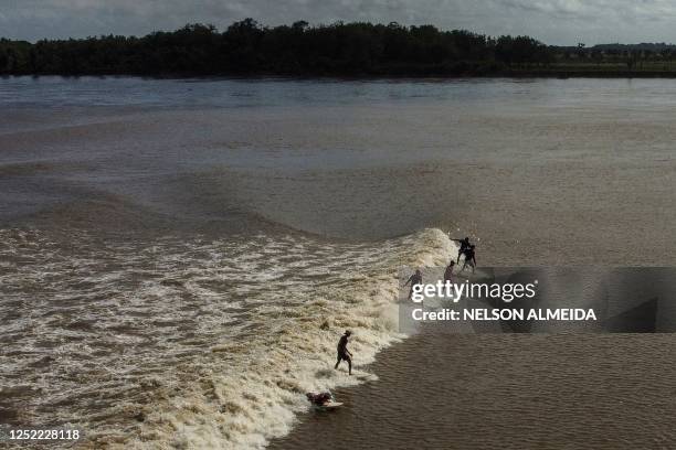 People surf on the wave of a tidal bore known as "Pororoca" at Mearim River in Arari, Maranhao state, Brazil, on April 22, 2023. - Pororoca, an...