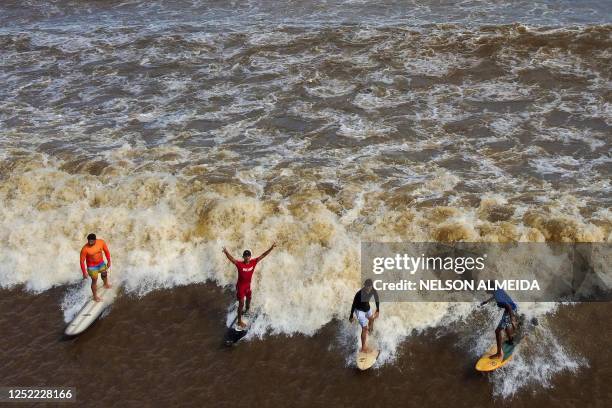 People surf on the wave of a tidal bore known as "Pororoca" at Mearim River in Arari, Maranhao state, Brazil, on April 22, 2023. - Pororoca, an...