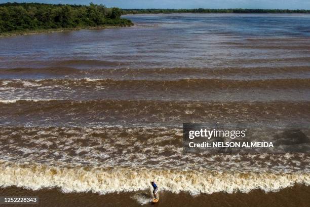 Man surfs on the wave of a tidal bore known as "Pororoca" at Mearim River in Arari, Maranhao state, Brazil, on April 22, 2023. - Pororoca, an admired...