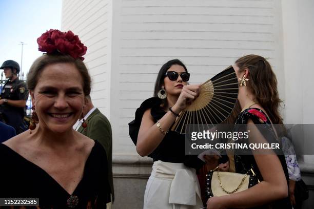 Visitors cool off with fans as they arrive for the Feria de Abril bullfighting festival at La Maestranza bullring in Seville on April 27, 2023. - An...