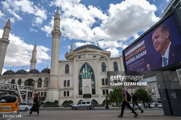 Pedestrians walk pass under a bilboad with the portrait of Turkish President Recep Tayyip Erdogan reading "right time, right man" with a mosque in...
