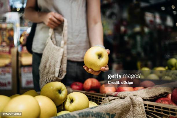 close up of young asian woman shopping for fresh organic fruits in farmer's market with a cotton mesh eco bag. environmentally friendly and zero waste concept - shopping stock-fotos und bilder