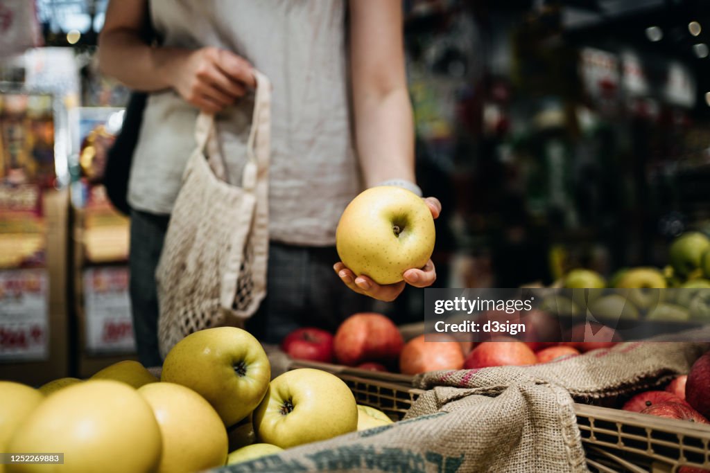 Close up of young Asian woman shopping for fresh organic fruits in farmer's market with a cotton mesh eco bag. Environmentally friendly and zero waste concept
