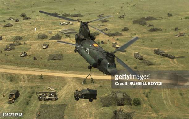 Royal Air Force Chinook helicopter carries an armored Land Rover as it flies over the camped NATO forces during training 09 June 1999. The...