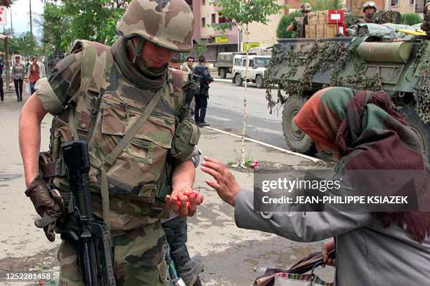 An old ethnic Albanian Kosovar woman hands some cherries 18 June 1999 to a French soldier part of the NATO-led KFOR troops in Mitrovica. France's...